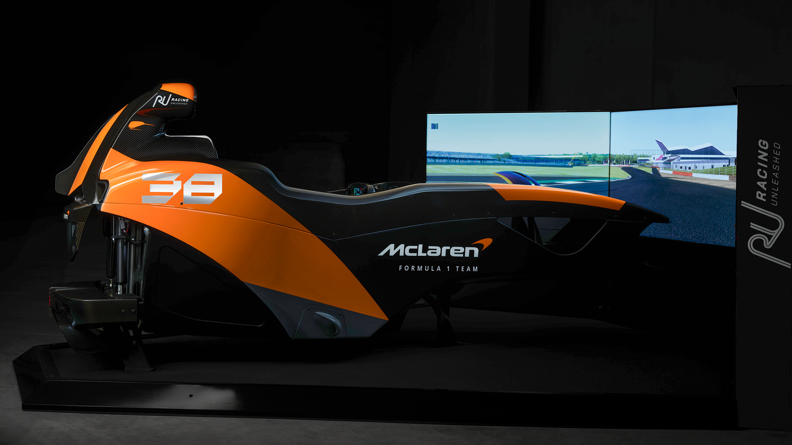 Ein McLaren-Rennsimulator von Racing Unleashed in orange-schwarzem Design vor Bildschirmen.